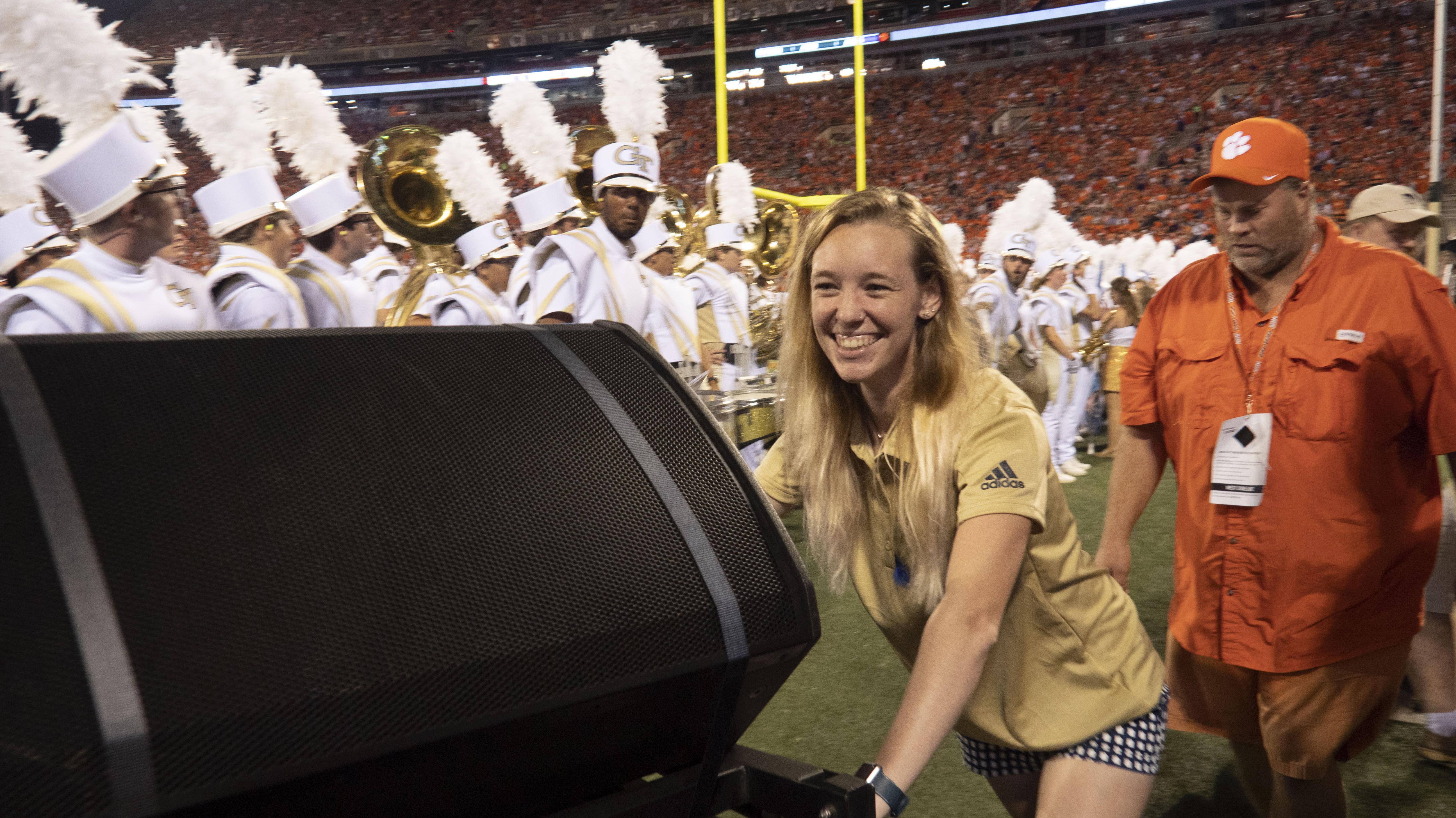 A staff assistant pushes a speaker off the field while the band sets up.
