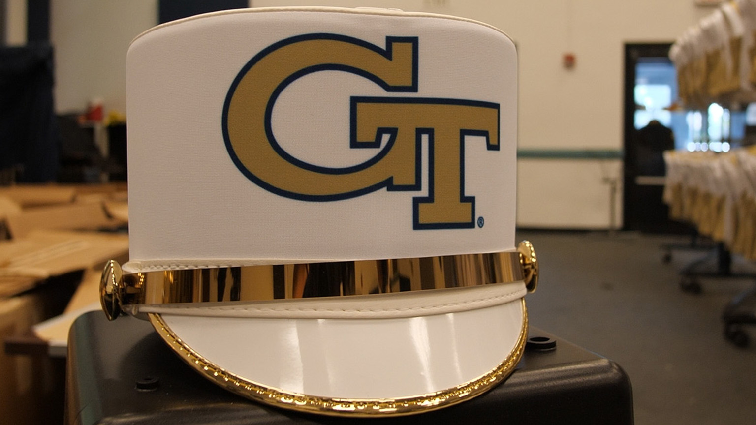 A close up of a band shako with racks of uniforms in the background.