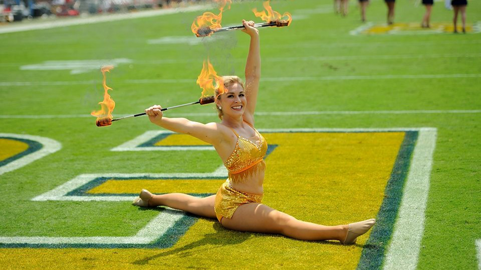A twirler doing a split with two burning batons in Georgia Tech's Endzone.