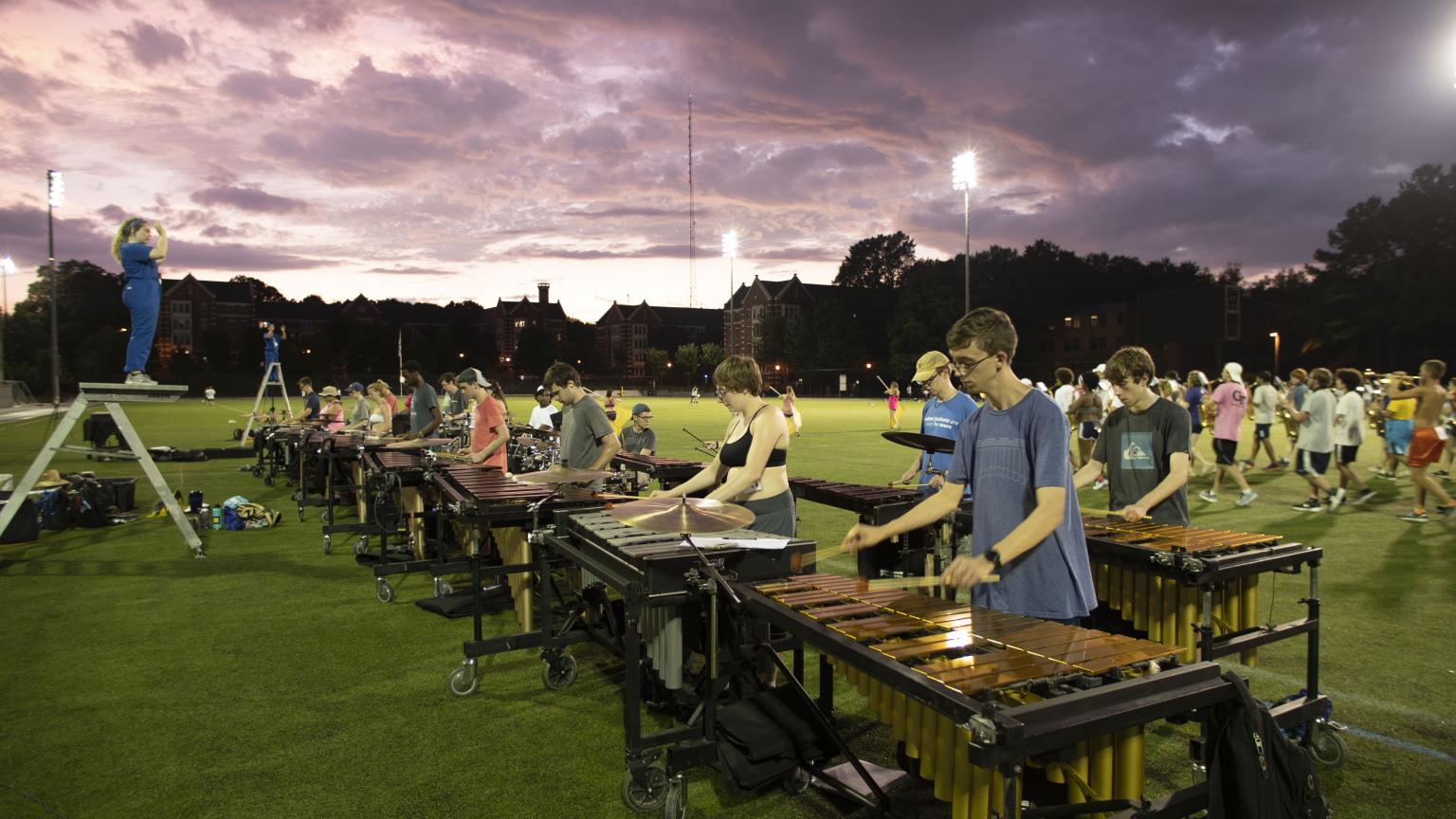 Percussion players practicing on Stamps field under an evening sky.